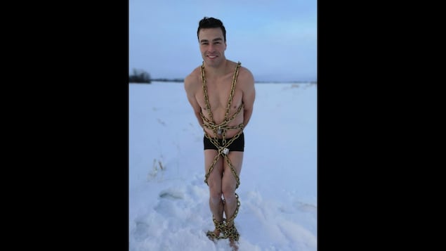 Roger Boucher en maillot de bain, debout et enchaîné, dans la neige. 