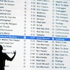 L'ombre d'un homme est visible devant un écran géant présentant une liste de nombreuses chansons disponibles sur une application.