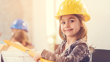 The picture features a young girl smiling, wearing a construction helmet.