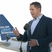 Andrew Scheer, devant la queue d'un avion sur laquelle on peut lire le slogan du Parti conservateur. 