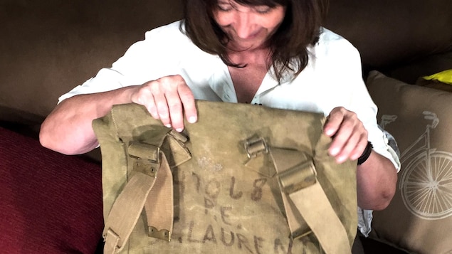 Une femme aux cheveux bruns contemple un vieux sac à dos militaire.