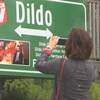 Une femme prend une photo d'une affiche indiquant le nom du village.