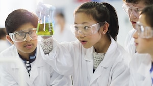 Les enfants regardent une jeune fille asiatique tenir une fiole avec une réaction chimique