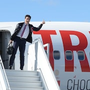 Justin Trudeau tient son pouce en l'air au haut de la rampe d'accès menant à l'avion du Parti libéral du Canada.