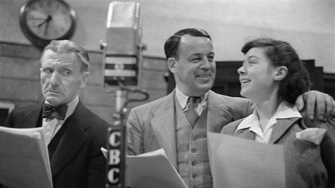 Dans un studio de radio, Hector Charland, Albert Duquesne, celui d'Alexis ainsi qu'Estelle Mauffette sont debout, côte à côte, leurs textes à la main, derrière un micro sur pied.