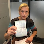 Kyle Kuchirka tient dans sa main un passeport dans lequel est écrit une note.