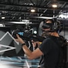 Un homme tient un fusil-jouet et porte un casque de réalité virtuelle. 