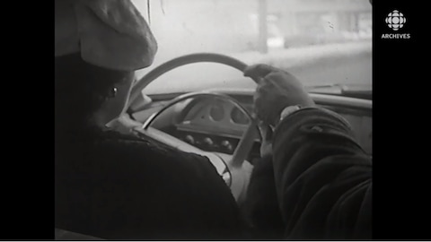 Femme vue de dos qui conduit et moniteur de conduite près d'elle avec une main sur le volant.