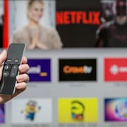 Une main tient une télécommande devant un écran où on voit les noms de Netflix et de Crave, entre autres.