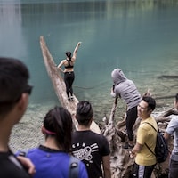 Une jeune femme fait une pose gracieuse sur un tronc à demi-submergé aux abords d'un lac du parc britanno-colombien de Joffre Lakes.