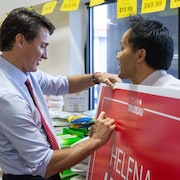 Justin Trudeau signe la pancarte électorale qu'un homme tient dans ses mains.