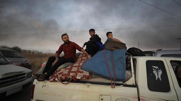 Des gens fuyant la ville de Ras al Ain sont assis sur leurs effets personnels à l'arrière d'un camion. 