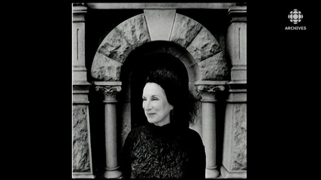 Margaret Atwood, souriante, posant devant un monument.
