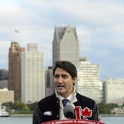 Justin Trudeau derrière un micro, avec la ville de Détroit en arrière-plan.