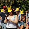 Plusieurs personnes marchent en regardant leur téléphone intelligent. Plusieurs d'entre elles portent un chapeau de Pikachu.