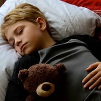 Un garçon d'environ 12 ans qui dort avec un ourson en peluche. 