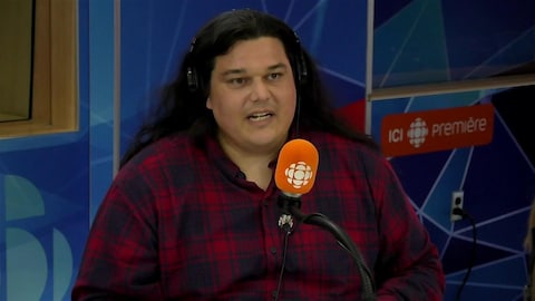 Alexis Wawanoloath derrière un micro dans un studio radio de Radio-Canada.