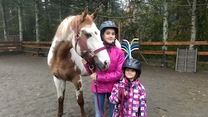 Deux fillettes sont dans un manège d'équitation et la plus grande tient un cheval. 