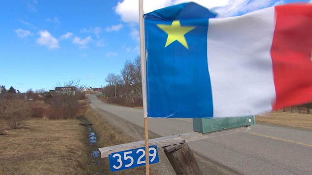 Drapeau de l'Acadie fixé à une boîte aux lettres en bordure d'une route.
