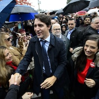 Justin Trudeau traverse la foule, sous la pluie, en serrant des mains et en souriant.