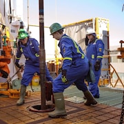 Trois employés du secteur pétrolier travaillent avec une machine de forage sur un navire.