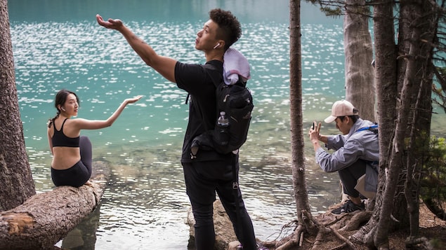 Des touristes tendent la main vers le ciel afin de percevoir s'il pleut aux abords d'un lac du parc britanno-colombien Joffre Lakes pendant qu'un autre prend une photo.