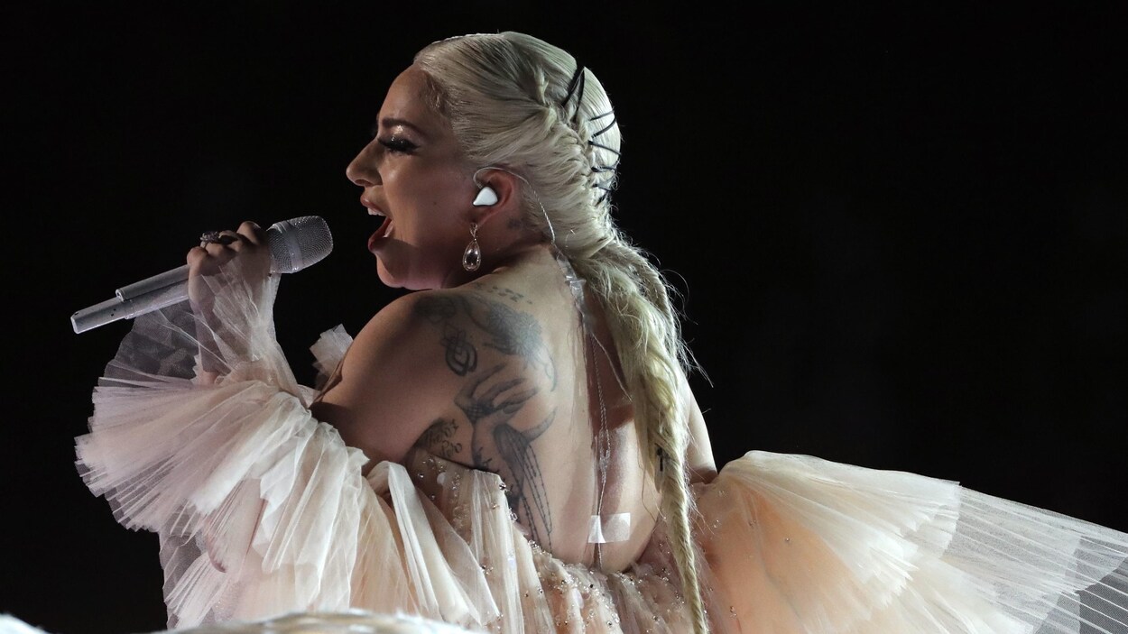 Lady Gaga, de profil sur scène, chante dans un microphone qu'elle tient à la main.