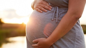Photo du ventre rond d'une femme enceinte devant un coucher de soleil.