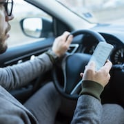Un homme utilise son cellulaire au volant de sa voiture.