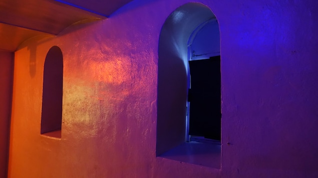 Un mur sur lequel on voit deux petites fenêtres éclairées par des lumières rouge et mauve.