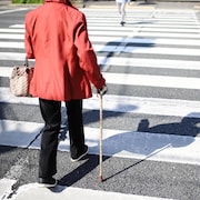 Une femme d'un certain âge traverse la rue à l'aide d'une canne.