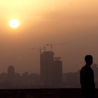 Le smog domine une ville au coucher du soleil. En contre-jour se trouve un homme en avant-plan.