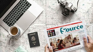 un journal, deux caméra, un laptop et un passeport posés sur une carte routière