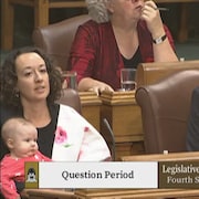Une femme tient un bébé dans ses bras. Elle est assise près de ses collègues élus de l'Assemblée législative de la Saskatchewan.