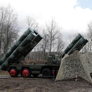 Quatre camions dont la cabine est recouverte d'un filet de camouflage déploient des tubes lance-missiles contenant des missiles S-400 russes. 