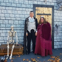Le couple costumé en vampire se trouve devant la porte du château, à côté d'un squelette enchaîné à un coffre.