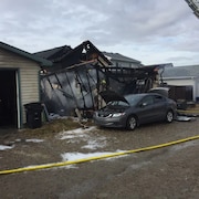 La carcasse d'une maison brûlée devant laquelle est stationnée une voiture.