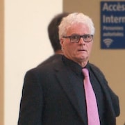 Yves Colosse Plamondon, un homme aux cheveux blancs, regarde la caméra. Il porte une cravate rose et un complet noir.