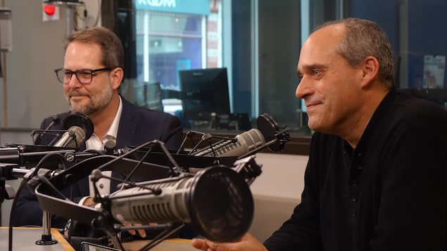 Deux hommes sourient devant des micros dans un studio de radio. 