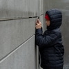 Un enfant filme avec son téléphone ce qu'il voit par la fente du mur.
