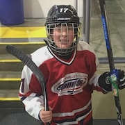Un jeune hockeyeur équipé pour jouer sourit à la caméra.