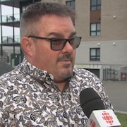 Louis Sauvé en entrevue à Radio-Canada devant un immeuble à logements.