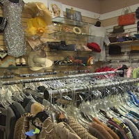 Des vêtements sont pendus à des cintres, et des chapeaux, foulard, sacs et autres articles sont en montre sur des présentoirs, dans un coin de la boutique.  