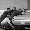 Policiers qui se cachent derrière une voiture, arme à la main.