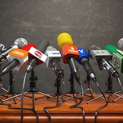 Des microphones de différents médias disposés sur un podium.
