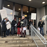 Environ dix manifestants tiennent des pancartes près de l'entrée d'un immeuble.
