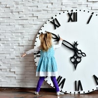 Une petite fille est en train de tourner l'aiguille d'une horloge surdimensionnée. 