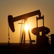 La silhouette d'un puits de pétrole devant un soleil couchant.