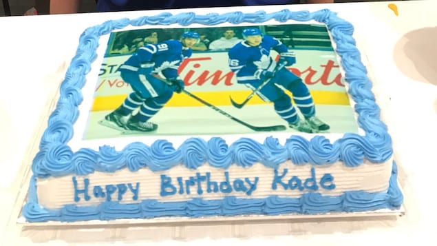 Un jeune garçon brun avec un t-shirt des Maple Leafs et un gâteau avec des joueurs de hockey en photo.