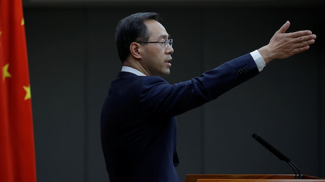 M. Feng, le bras gauche levé, lors d'un point de presse devant le drapeau chinois.